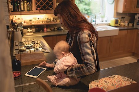 simsearch:6109-08390041,k - Mother using digital tablet while carrying her baby in kitchen at home Stock Photo - Premium Royalty-Free, Code: 6109-08944562