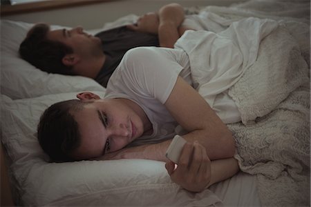 Man checking his mobile phone while lying on the bed with his gay partner in bedroom Stock Photo - Premium Royalty-Free, Code: 6109-08944648