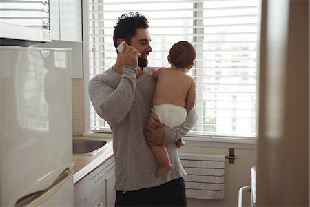 simsearch:6116-07236010,k - Father talking on mobile phone while holding his baby in kitchen Stock Photo - Premium Royalty-Free, Code: 6109-08944669