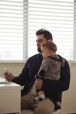 simsearch:6116-07236010,k - Father holding his baby while using mobile phone at desk at home Stock Photo - Premium Royalty-Free, Code: 6109-08944709