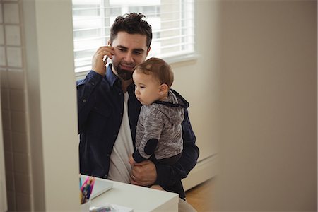 simsearch:6116-07236010,k - Father talking on mobile phone while holding his baby at home Stock Photo - Premium Royalty-Free, Code: 6109-08944711