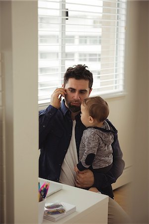 simsearch:6116-07236010,k - Father talking on mobile phone while holding his baby at home Stock Photo - Premium Royalty-Free, Code: 6109-08944712