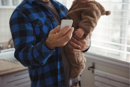 simsearch:6116-07236010,k - Mid section of father using mobile phone while holding his baby in kitchen Stock Photo - Premium Royalty-Free, Code: 6109-08944735