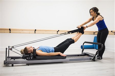 simsearch:6108-06906954,k - Female trainer assisting woman with stretching exercise on reformer in gym Stock Photo - Premium Royalty-Free, Code: 6109-08944803