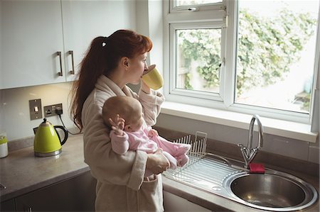 simsearch:6102-08566788,k - Mother carrying baby while drinking coffee in domestic kitchen Stock Photo - Premium Royalty-Free, Code: 6109-08945237