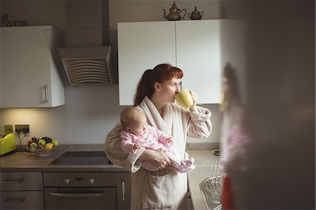 simsearch:6102-08566788,k - Mother carrying baby while having coffee in domestic kitchen Stock Photo - Premium Royalty-Free, Code: 6109-08945236