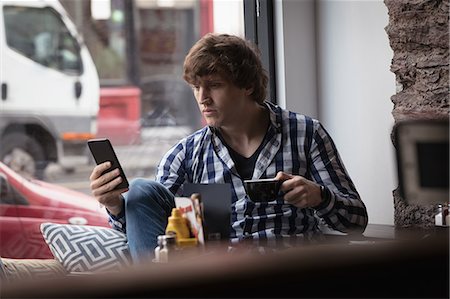 simsearch:6109-08690411,k - Man using mobile phone while having coffee in Café Stock Photo - Premium Royalty-Free, Code: 6109-08953870