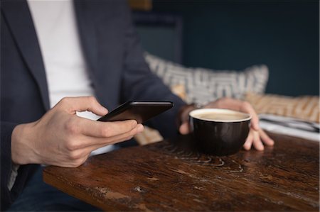simsearch:6109-08690411,k - Mid section of man using mobile phone while having coffee in Café Stock Photo - Premium Royalty-Free, Code: 6109-08953879