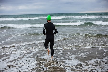 simsearch:400-04535435,k - Rear view of athlete in wet suit running towards the sea Stock Photo - Premium Royalty-Free, Code: 6109-08928473