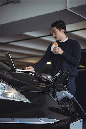 Man using laptop while charging electric car in garage Stock Photo - Premium Royalty-Free, Code: 6109-08928997