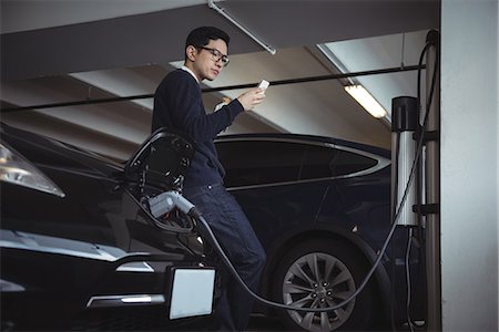 Man using mobile phone while charging electric car in garage Stock Photo - Premium Royalty-Free, Code: 6109-08928999