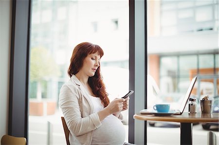 simsearch:6109-08700458,k - Pregnant businesswoman using mobile phone in office cafeteria Stock Photo - Premium Royalty-Free, Code: 6109-08929289