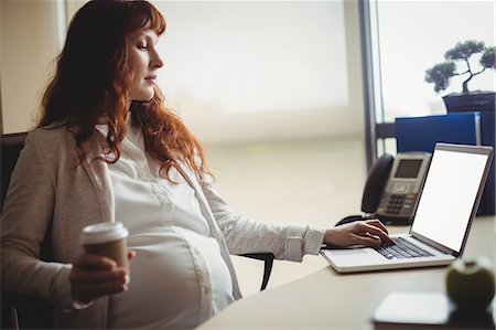 simsearch:6109-08700458,k - Pregnant businesswoman using laptop while having coffee in office Stock Photo - Premium Royalty-Free, Code: 6109-08929322