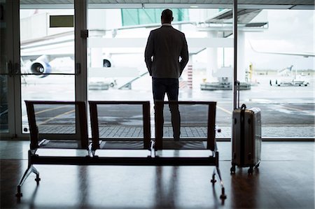 simsearch:400-03938985,k - Rear view of businessman with luggage looking through glass window at airport Foto de stock - Sin royalties Premium, Código: 6109-08929445