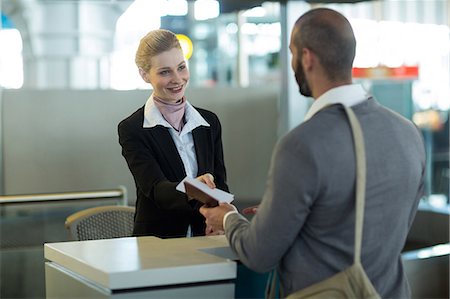simsearch:400-03938985,k - Airline check-in attendant handing passport to commuter at counter in airport terminal Foto de stock - Sin royalties Premium, Código: 6109-08929411