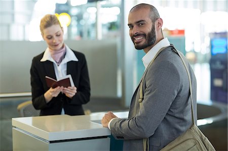 simsearch:400-03938985,k - Smiling commuter standing at counter while attendant checking his passport at airport terminal Foto de stock - Sin royalties Premium, Código: 6109-08929412
