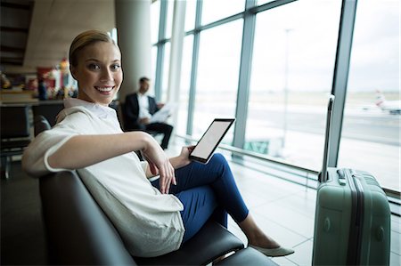 Portrait of female commuter with digital tablet sitting in waiting area at airport Stock Photo - Premium Royalty-Free, Code: 6109-08929568