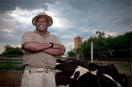 Black farmer, smiles at camera, with cows in the background Stock Photo - Premium Royalty-Free, Code: 6110-09134245