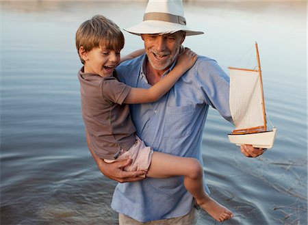 Smiling grandfather and grandson with toy sailboat wading in lake Stock Photo - Premium Royalty-Free, Code: 6113-06498465