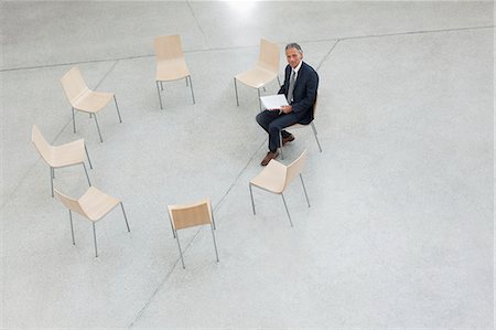 simsearch:6113-07243220,k - Portrait of smiling businessman sitting in circle of chairs Stock Photo - Premium Royalty-Free, Code: 6113-06498799