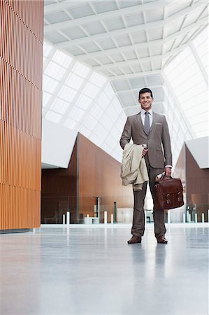 Portrait of smiling businessman holding coat and briefcase in lobby Stock Photo - Premium Royalty-Free, Code: 6113-06498870