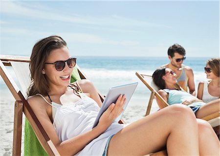 Happy woman using digital tablet in lounge chair on beach Stock Photo - Premium Royalty-Free, Code: 6113-06899249