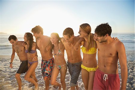 simsearch:6113-06899255,k - Friends in bikinis and swim trunks hugging and walking on beach Stock Photo - Premium Royalty-Free, Code: 6113-06899286