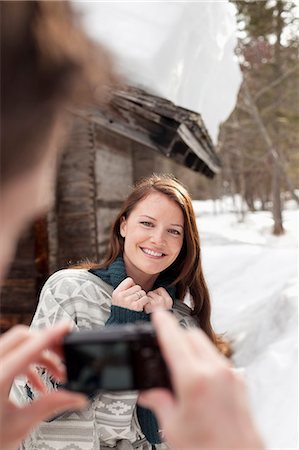 Man photographing smiling woman in snow outside cabin Stock Photo - Premium Royalty-Free, Code: 6113-06899449