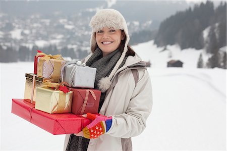 Portrait of smiling woman carrying Christmas gifts in snowy field Stock Photo - Premium Royalty-Free, Code: 6113-06899485