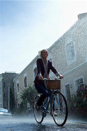 person in a basket of a bike - Happy woman riding bicycle in rainy street Stock Photo - Premium Royalty-Free, Code: 6113-06899587