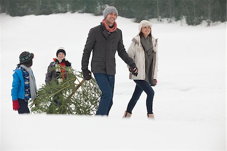 simsearch:6113-06899473,k - Smiling family dragging fresh Christmas tree in snowy field Stock Photo - Premium Royalty-Free, Code: 6113-06899500