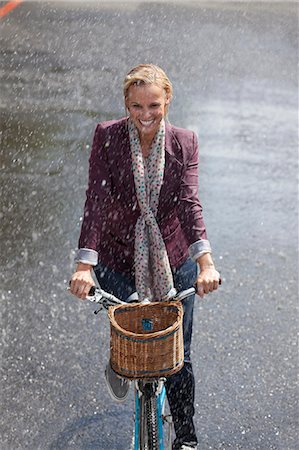 person in a basket of a bike - Happy woman riding bicycle in rainy street Stock Photo - Premium Royalty-Free, Code: 6113-06899665