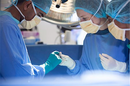 surgical gown - Surgeons bent over patient on operating table Photographie de stock - Premium Libres de Droits, Code: 6113-06908214