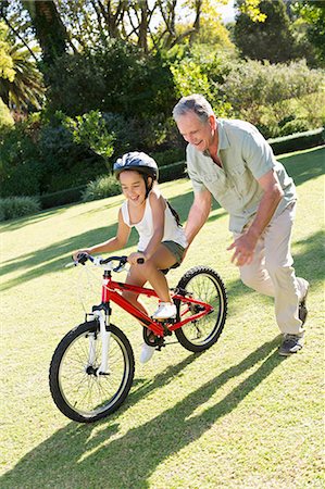 retired happy - Older man teaching granddaughter to ride bicycle Stock Photo - Premium Royalty-Free, Code: 6113-06909421