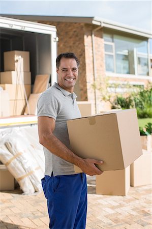 Portrait of smiling man holding cardboard box near moving van in driveway Stock Photo - Premium Royalty-Free, Code: 6113-07147162