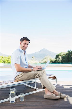 Man using laptop on lounge chair at poolside Stock Photo - Premium Royalty-Free, Code: 6113-07147492