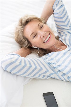 Older woman listening to earphones on bed Stock Photo - Premium Royalty-Free, Code: 6113-07159642