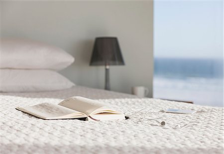 Book and glasses on bed in modern bedroom with ocean view Photographie de stock - Premium Libres de Droits, Code: 6113-07160195