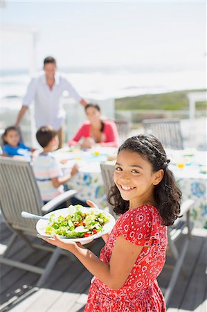family in a table - Smiling girl carrying salad bowl on sunny patio Stock Photo - Premium Royalty-Free, Code: 6113-07242561