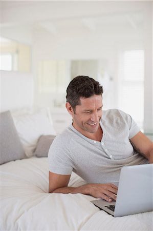 Man using laptop on bed Stock Photo - Premium Royalty-Free, Code: 6113-07242661