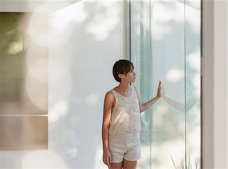 Pensive woman standing at sunny window Stock Photo - Premium Royalty-Free, Code: 6113-07542739