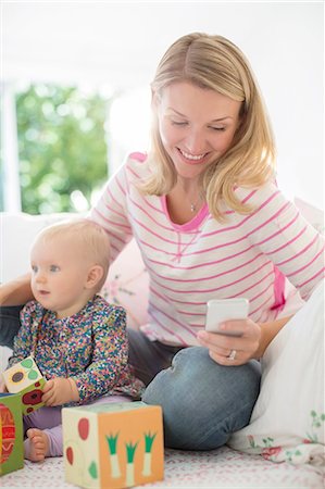 Mother playing with baby girl and checking cell phone Stock Photo - Premium Royalty-Free, Code: 6113-07543253