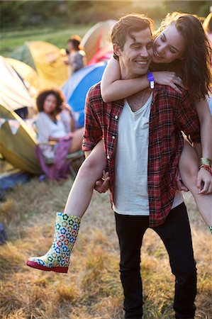 Man piggybacking woman outside tents at music festival Stock Photo - Premium Royalty-Free, Code: 6113-07564772