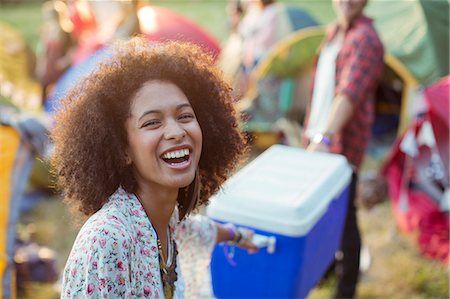 Portrait of laughing woman helping man carry cooler outside tents at music festival Stock Photo - Premium Royalty-Free, Code: 6113-07564850