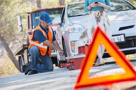 simsearch:700-03686142,k - Roadside mechanic changing tire behind warning triangle Stock Photo - Premium Royalty-Free, Code: 6113-07565004