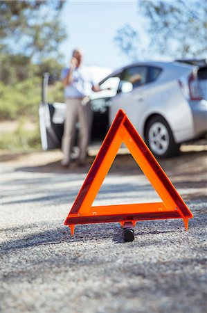 Man talking on cell phone at roadside behind warning triangle Stock Photo - Premium Royalty-Free, Code: 6113-07565012