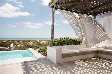 simsearch:6113-07147822,k - Curtains blowing in wind on luxury poolside patio overlooking ocean Photographie de stock - Premium Libres de Droits, Code: 6113-07565184