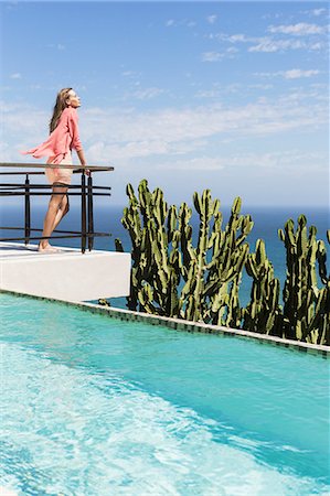 Woman basking in sun on poolside balcony overlooking ocean Stock Photo - Premium Royalty-Free, Code: 6113-07565192