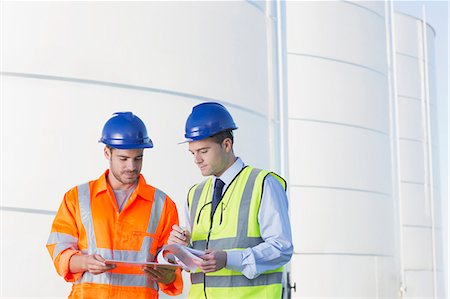 simsearch:6113-07565342,k - Workers reviewing paperwork next to silage storage towers Stock Photo - Premium Royalty-Free, Code: 6113-07565332