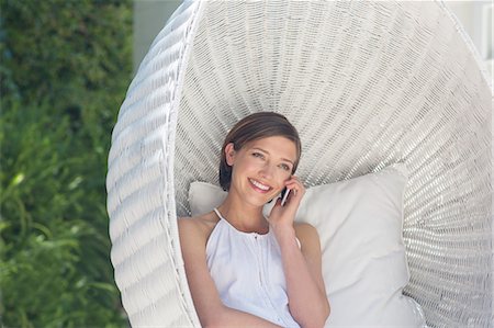 simsearch:6113-07790529,k - Woman talking on cell phone in hanging wicker chair outdoors Stock Photo - Premium Royalty-Free, Code: 6113-07790554